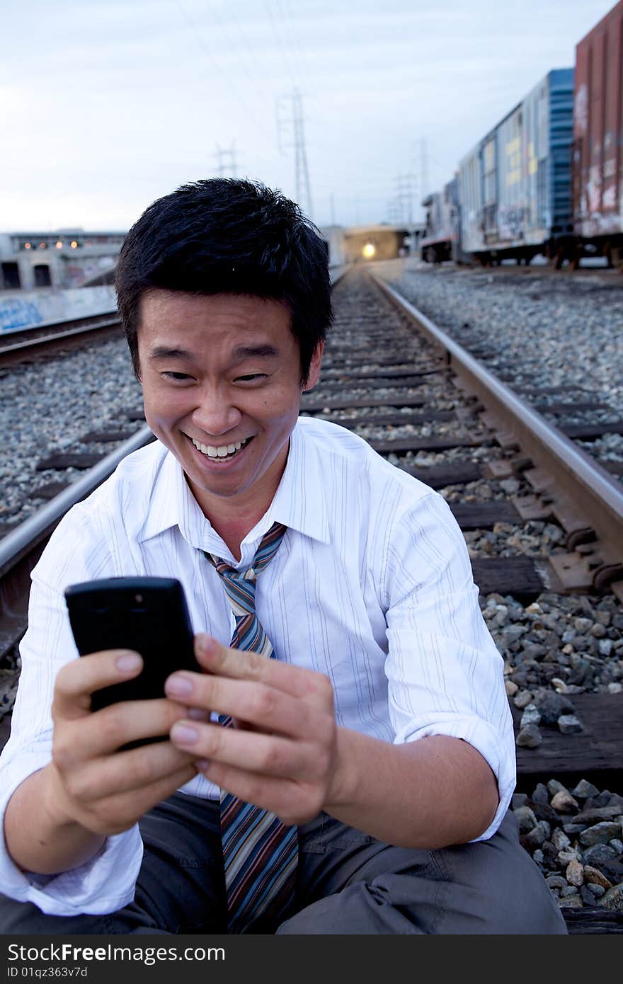 An Asian man sitting on the train tracks making a call. An Asian man sitting on the train tracks making a call