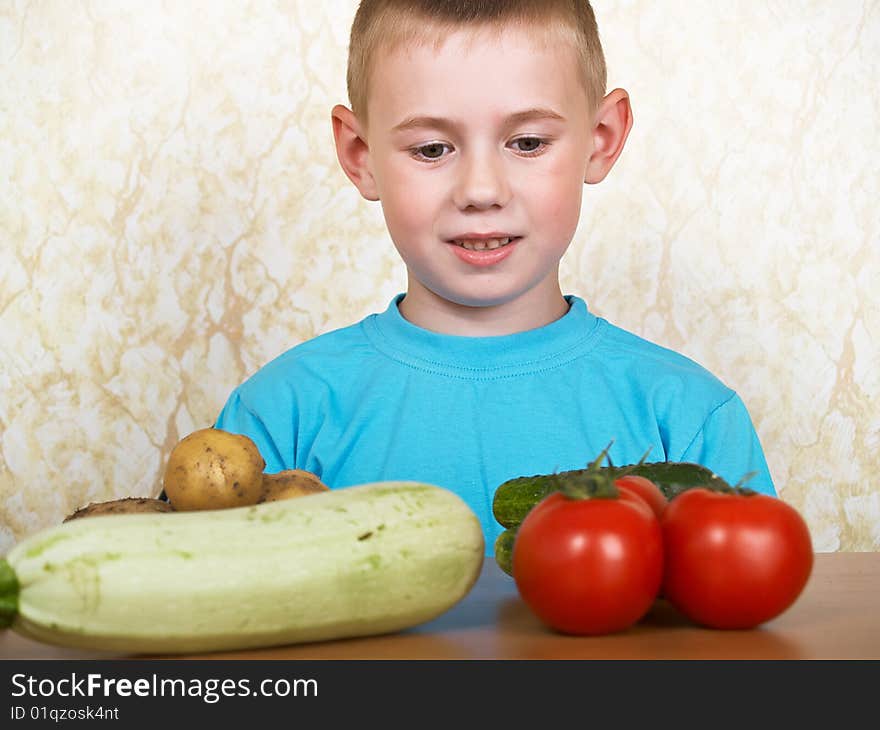 The boy sits at a table with vegetables. The boy sits at a table with vegetables