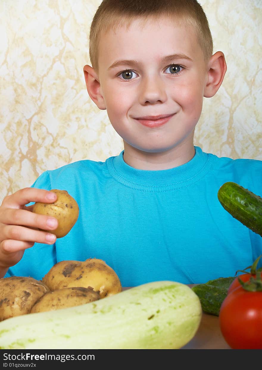 The boy sits at a table with vegetables. The boy sits at a table with vegetables