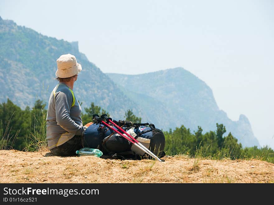 Tired hiker relaxes on a hill and enjoys landscape