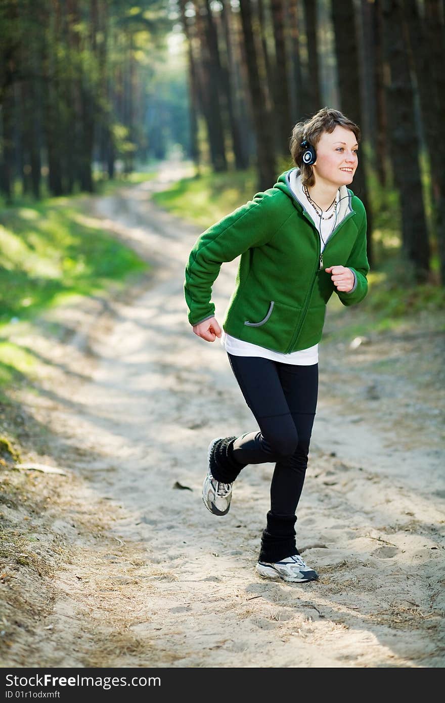 Young girl runner in the forest while listening to music