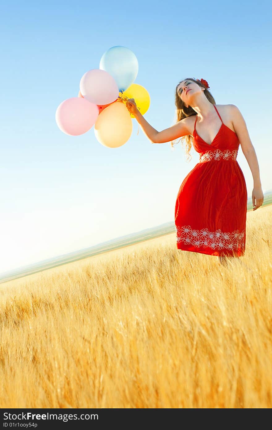 Young woman in a wheat field holding colorful balloons. Young woman in a wheat field holding colorful balloons