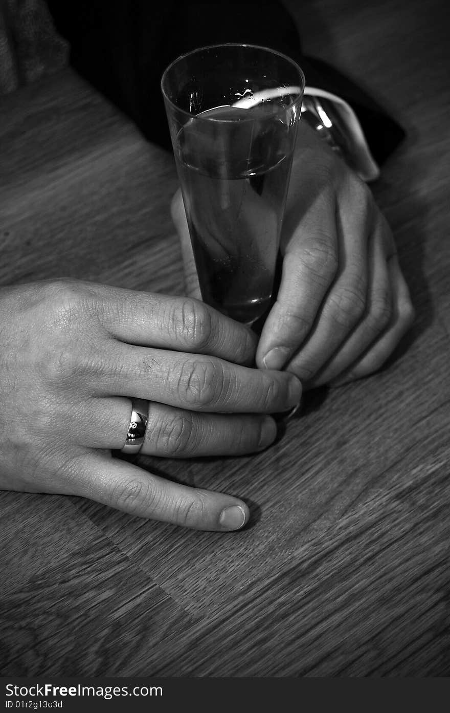 A pair of hands holding a drink glass. A ring on one of the fingers. watch is visable. A pair of hands holding a drink glass. A ring on one of the fingers. watch is visable