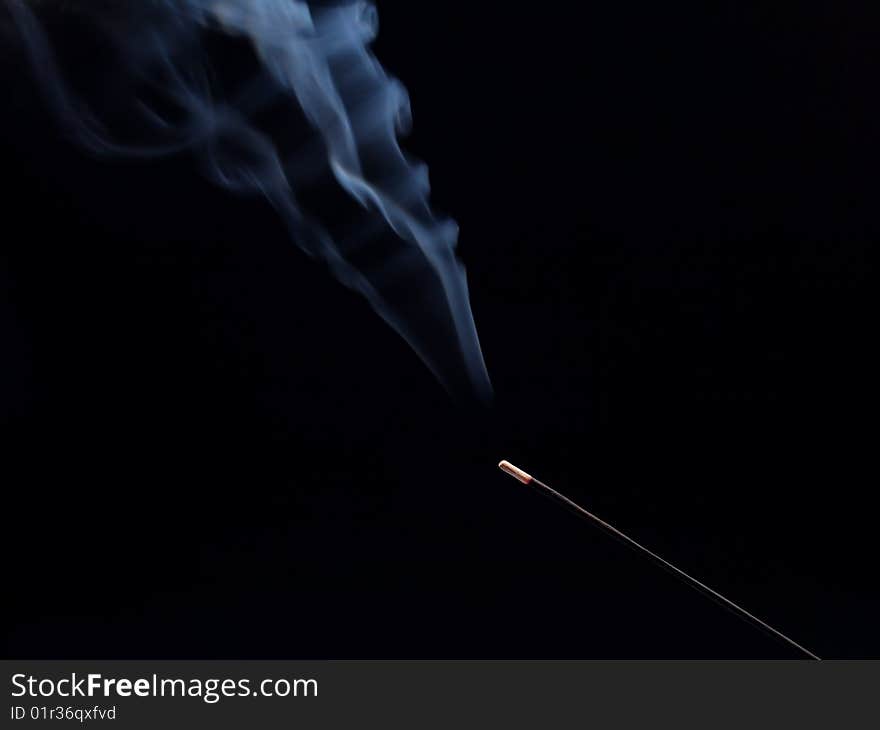 Smouldering aroma stick on a black background. There is a smoke above the stick. Smouldering aroma stick on a black background. There is a smoke above the stick.