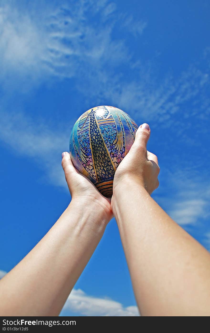 Easter egg in hands against the sky