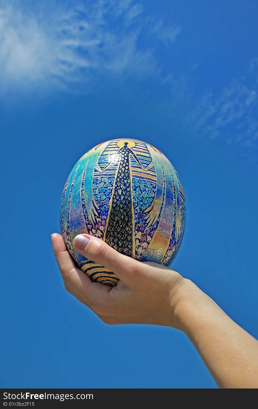 Easter egg in hands against the sky