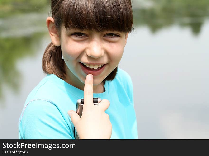 Portrait of nice young smiling girl handing mobile phone on nature background