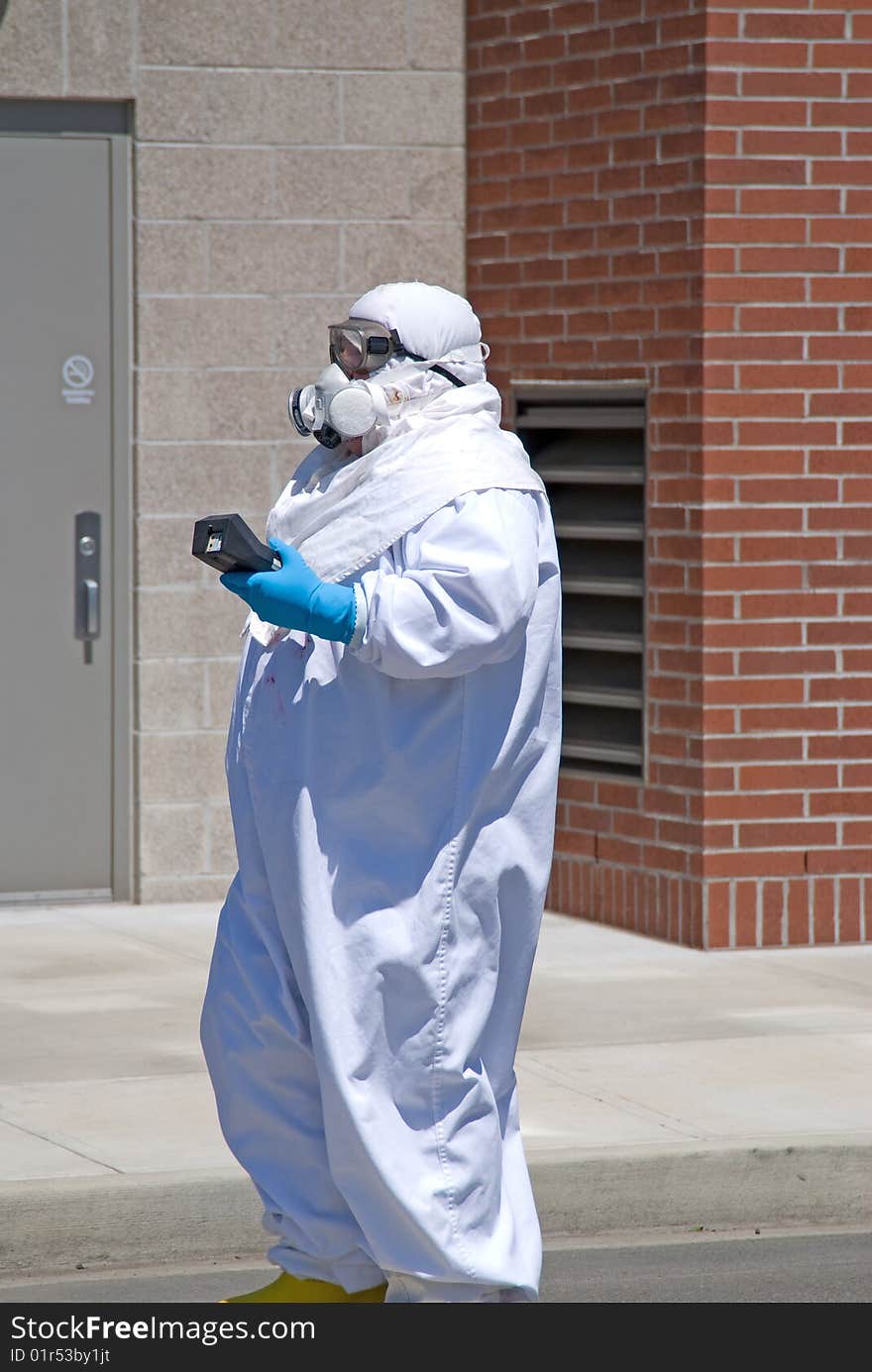 A man walking down a street in the Northwest in a suit designed to keep germs out holding a medical instrument. A man walking down a street in the Northwest in a suit designed to keep germs out holding a medical instrument.