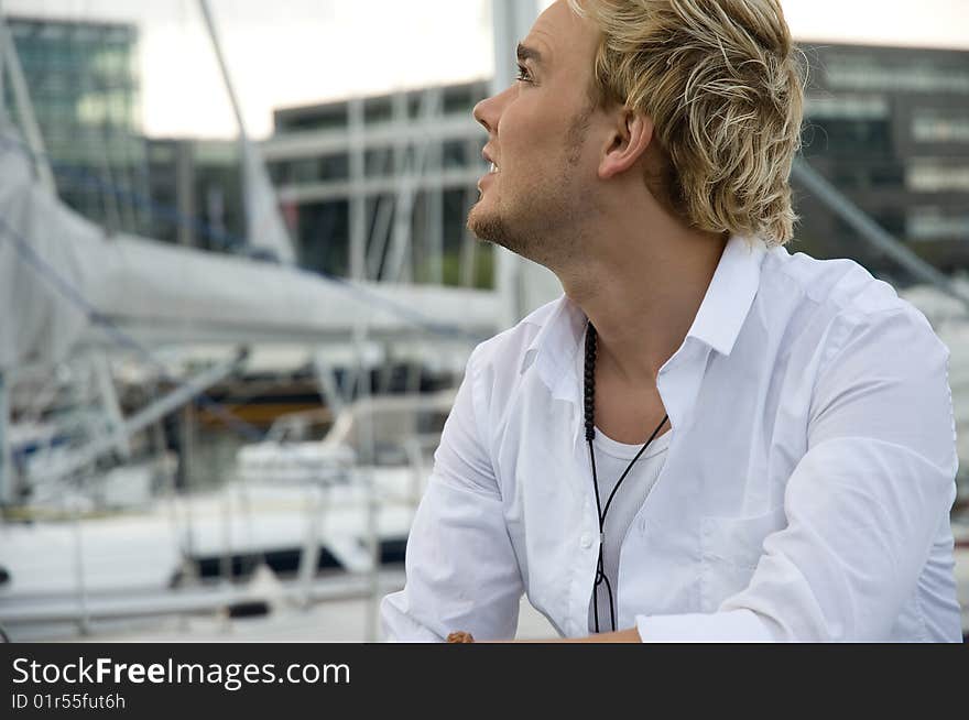 Young man sitting near some yachts at a yachtclub. Young man sitting near some yachts at a yachtclub