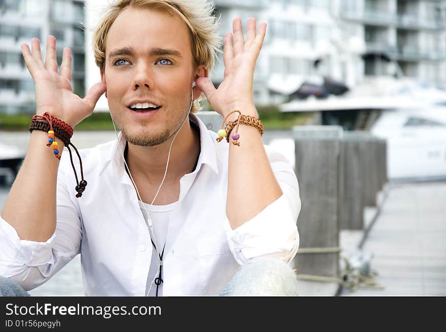 Young man sitting near some yachts at a yacht club listening to music. Young man sitting near some yachts at a yacht club listening to music