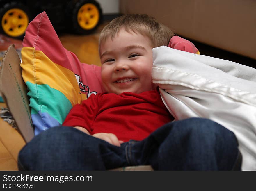 A young boy sitting in a box and smiling while holding his blanket. A young boy sitting in a box and smiling while holding his blanket.