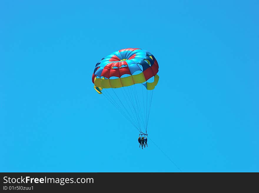 A multicolored parasail at an angle with three passengers. A multicolored parasail at an angle with three passengers.