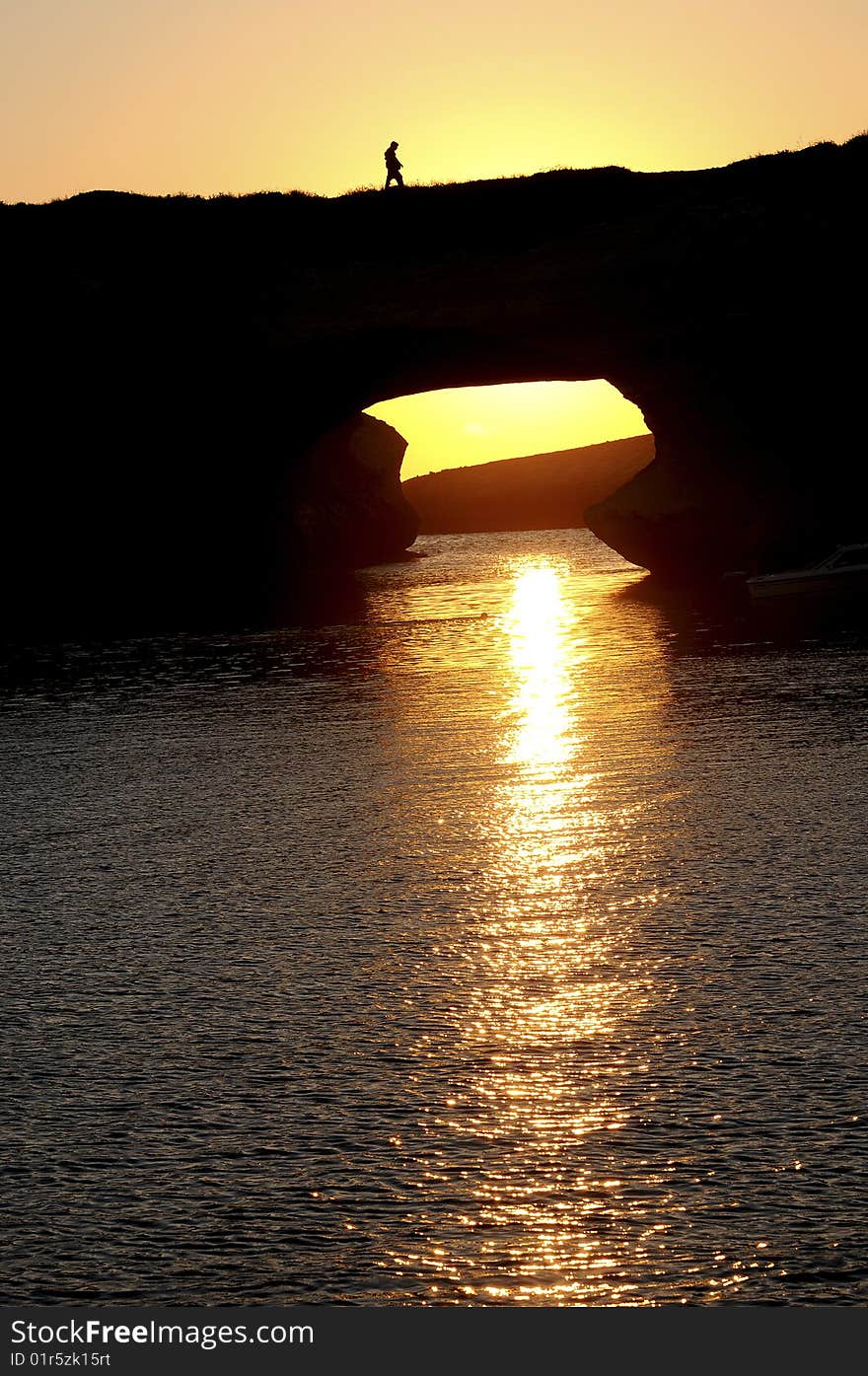 Sunset over the sea on mediterranean island, somebody is walking over a rocky arch. Sunset over the sea on mediterranean island, somebody is walking over a rocky arch