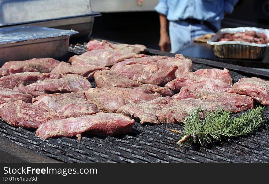 Steaks are cooking on an outdoor grill. Rosemary is also on the grill. Steaks are cooking on an outdoor grill. Rosemary is also on the grill.