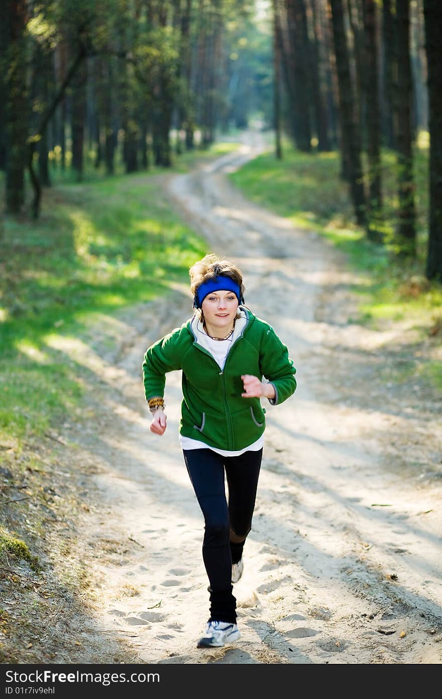 Pretty young girl runner in the forest while listening to music.