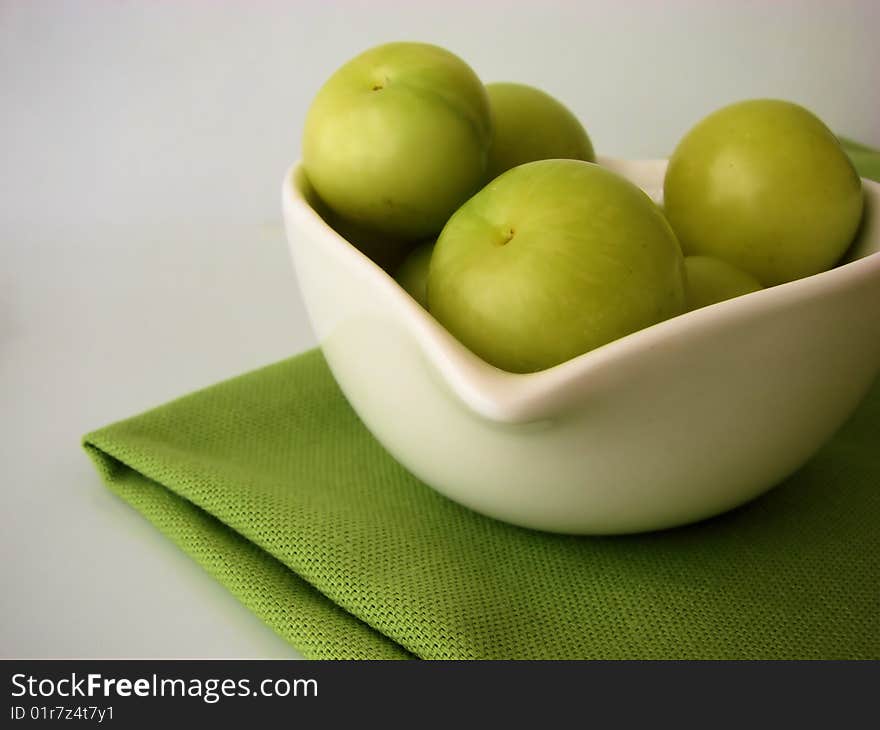 Green plums in a white bowl