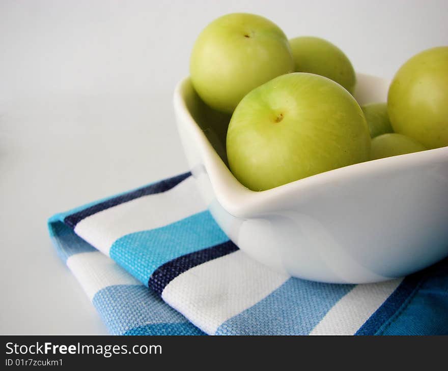 Green plums in a white bowl