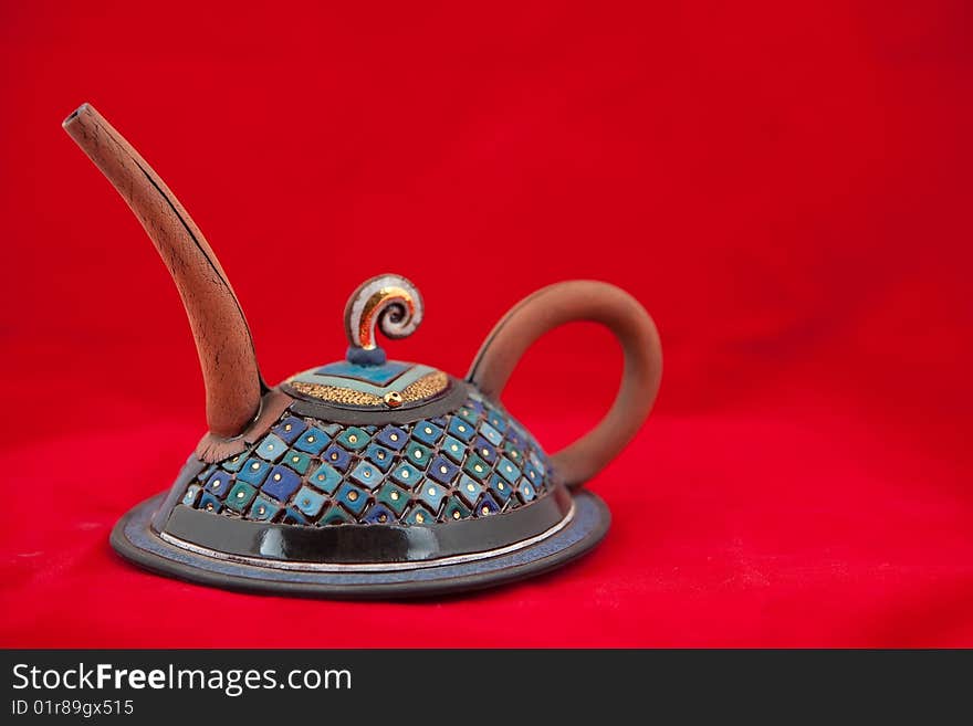 Solitary clay hand crafted very ornate teapot on red background. Solitary clay hand crafted very ornate teapot on red background