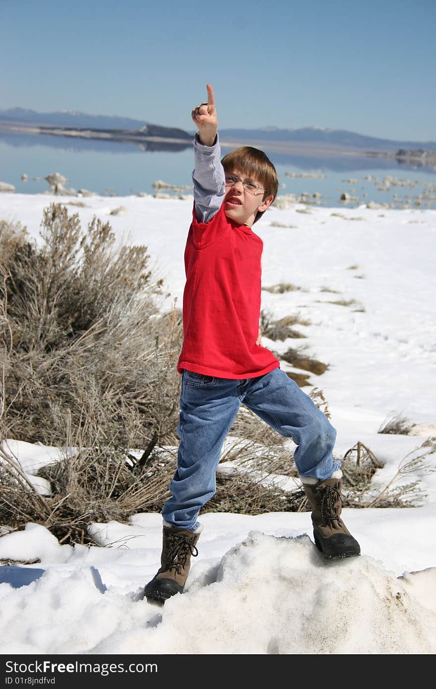 Boy standing on a rock in front of a lake in the snow pointing up. Boy standing on a rock in front of a lake in the snow pointing up