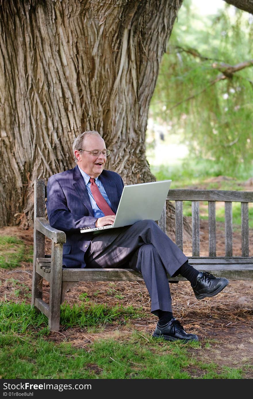 An excited man looks at his laptop on a park bench