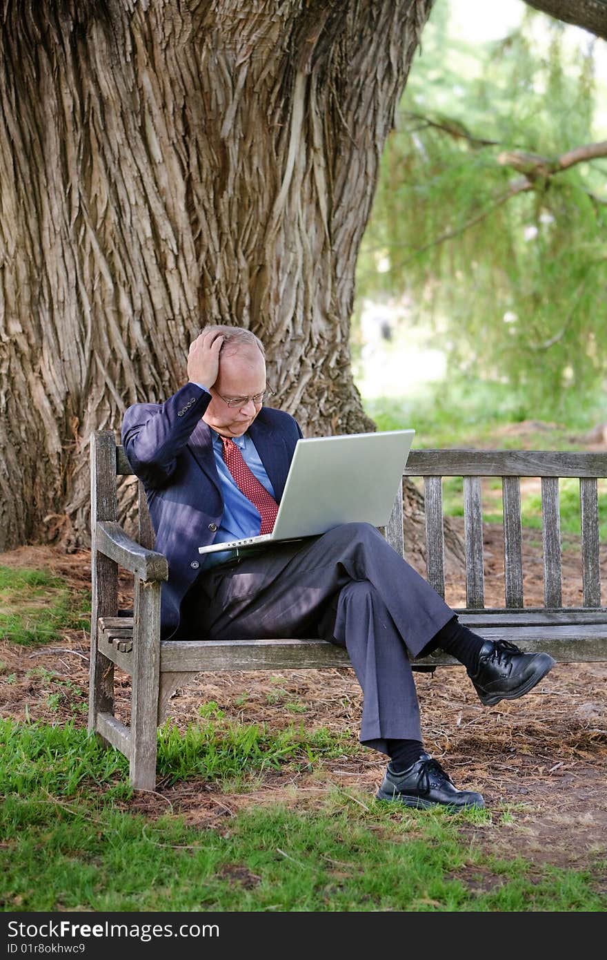 An older man becomes frustrated while using his laptop computer in the park. An older man becomes frustrated while using his laptop computer in the park