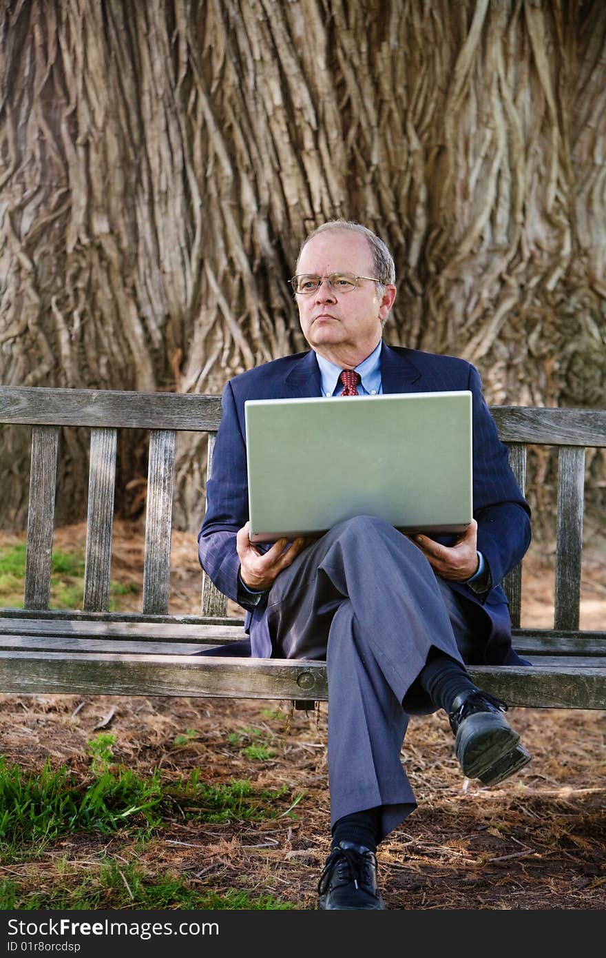 An older business man looks into the distance while working on his laptop computer. An older business man looks into the distance while working on his laptop computer