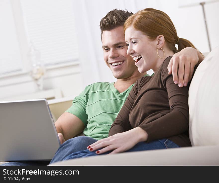 A young and attractive couple sitting together and viewing a laptop screen. They are smiling and laughing. Horizontally framed photo. A young and attractive couple sitting together and viewing a laptop screen. They are smiling and laughing. Horizontally framed photo.