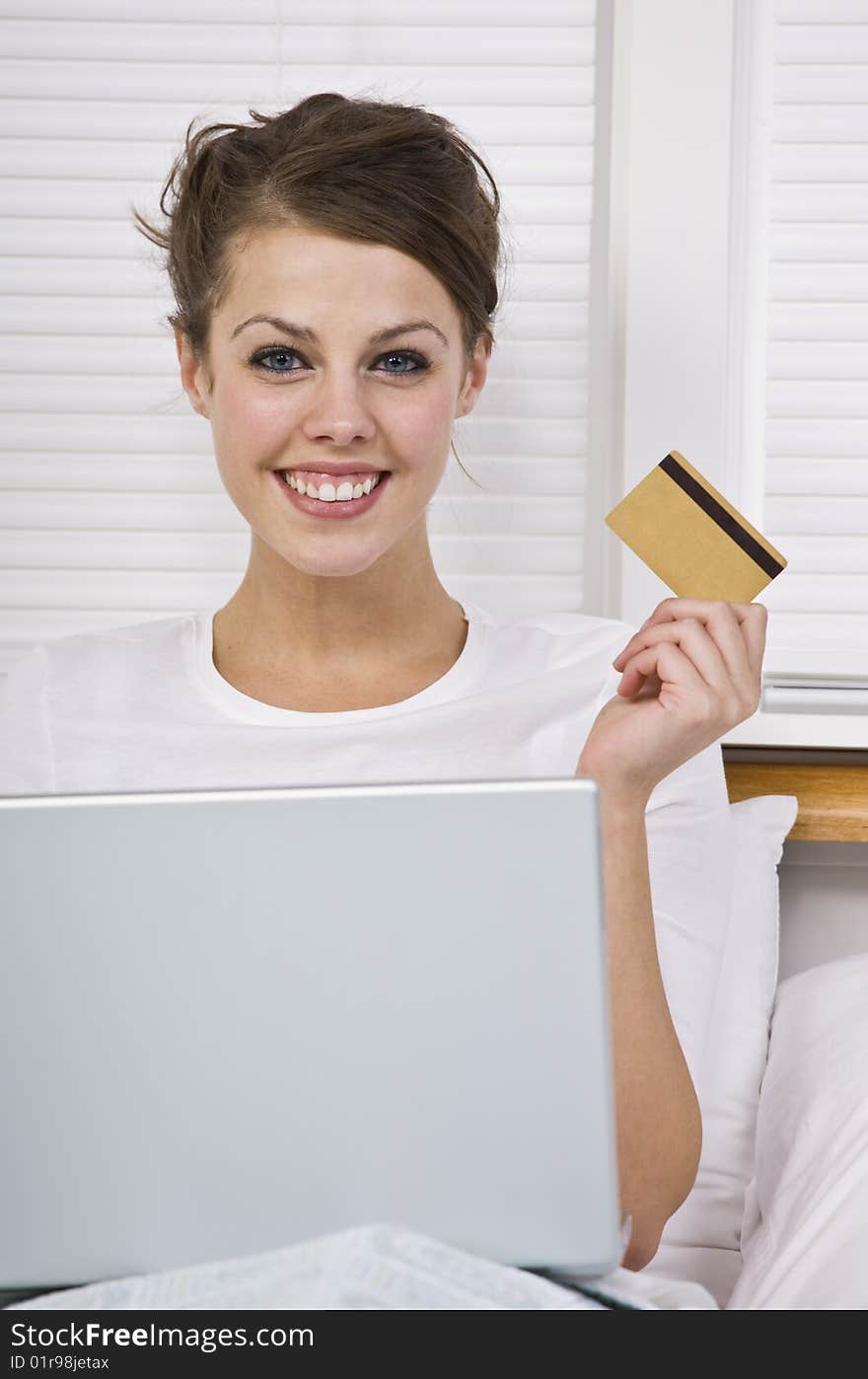 Attractive woman holding credit card with laptop and smiling at the camera. Vertically framed. Attractive woman holding credit card with laptop and smiling at the camera. Vertically framed.