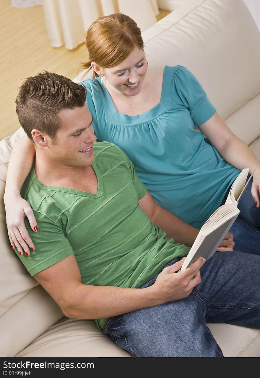 An attractive young couple seated on a couch together and reading from a book.  They are smiling. Vertically framed shot. An attractive young couple seated on a couch together and reading from a book.  They are smiling. Vertically framed shot.