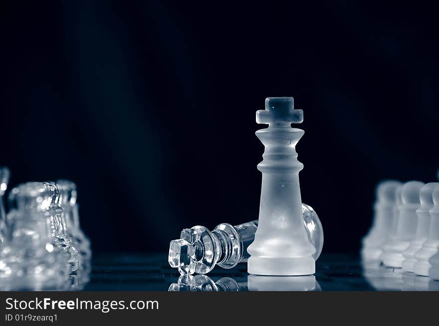 Checkmate with glass king lying on chessboard against black background. Checkmate with glass king lying on chessboard against black background