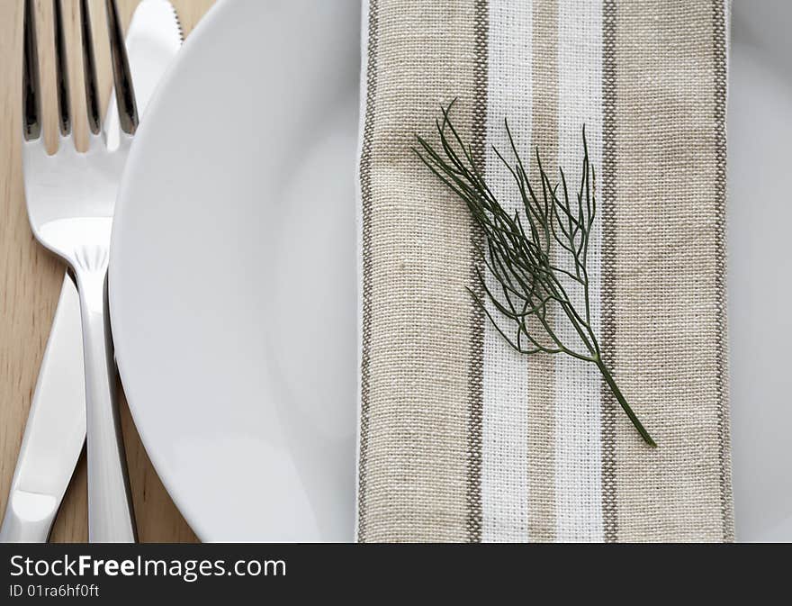 Serving of white plates, forks, knives, cloth napkins with a sprig of dill. Serving of white plates, forks, knives, cloth napkins with a sprig of dill