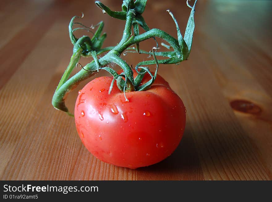 1 red tomato on vine, set on wooden table.