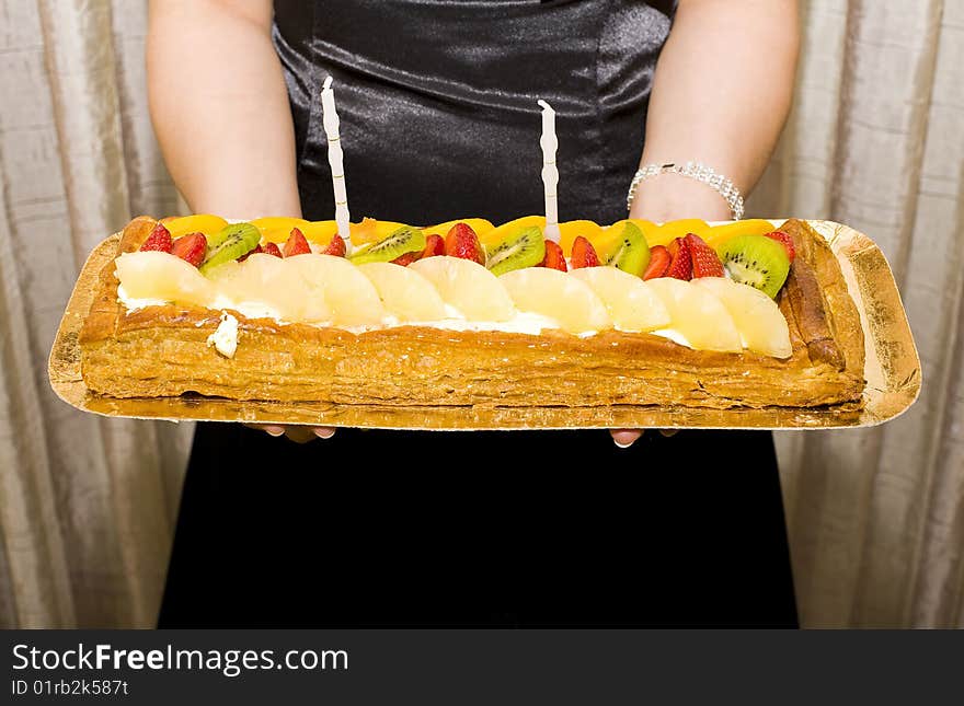 A birthday cake with candles and strawberries and pineapple and kiwi