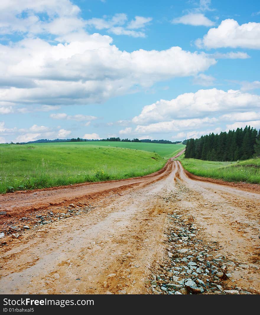 Rural road with gravel with green lawn and blue sky with clouds