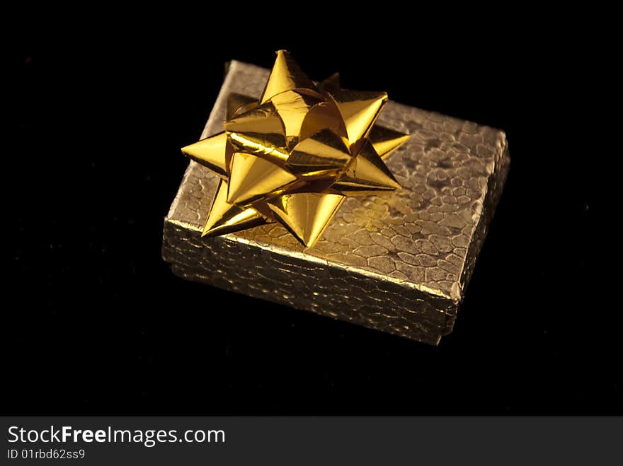 A small textured silver box with a gold bow on a flat black surface. A small textured silver box with a gold bow on a flat black surface