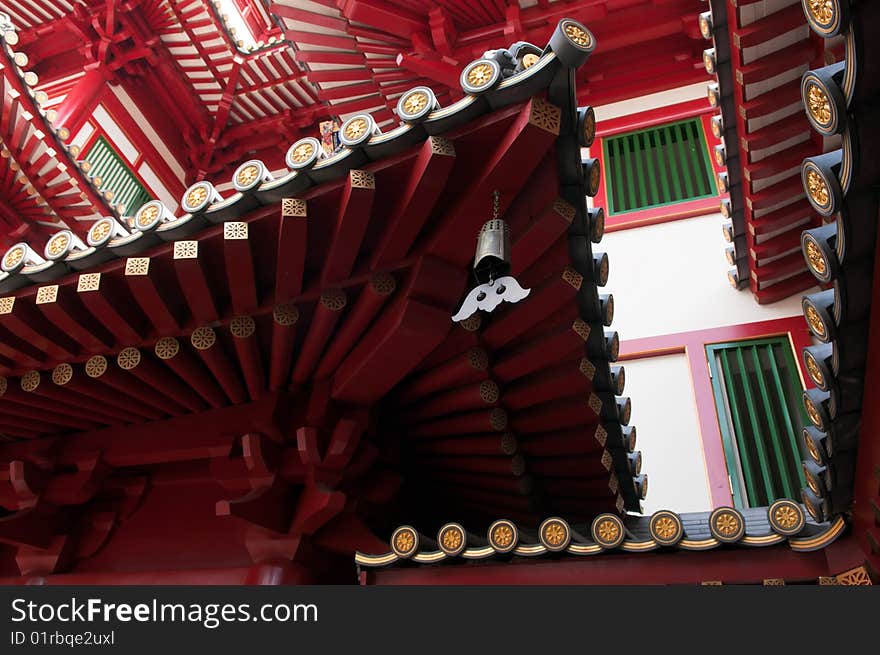 A brass bell with a bat shaped clapper hanging rom the turned up corner of the roof of a Buddhist temple build in classical Chinese architectural style, in Chinatown, Singapore. A brass bell with a bat shaped clapper hanging rom the turned up corner of the roof of a Buddhist temple build in classical Chinese architectural style, in Chinatown, Singapore