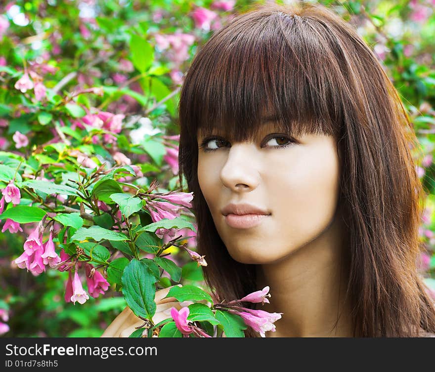 Young woman near blossoming flowers. Summer garden. Young woman near blossoming flowers. Summer garden.