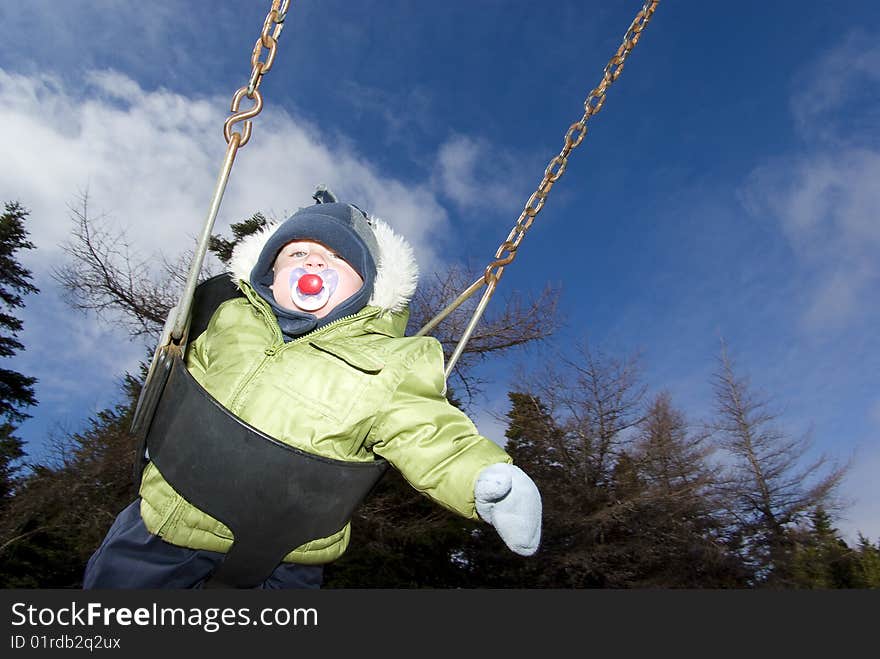 Baby swinging on playground during cold spring day