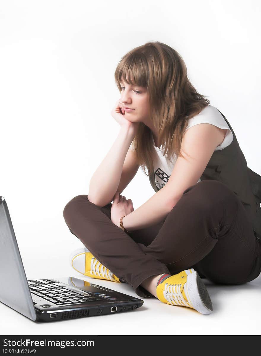 Casual teenage girl on a laptop on a white background working on the floor