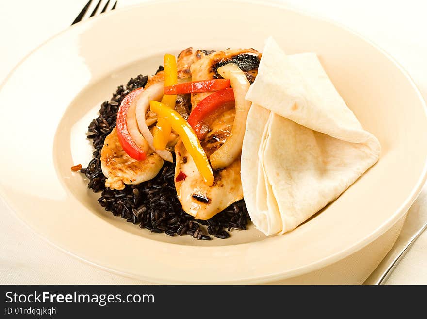 A healthy meal of chicken breast served on black rice with tortilla