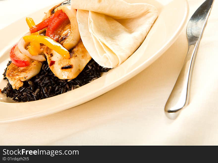 A healthy meal of chicken breast served on black rice with tortilla