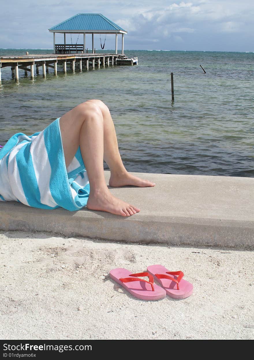 Pink sandals at the feet of a sunbather at the water's edge in the Gulf of Mexico.