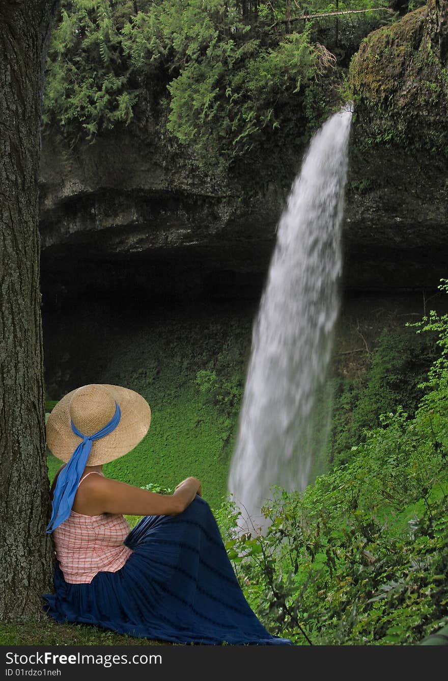 A woman sitting on a small hill looking at a waterfall. A woman sitting on a small hill looking at a waterfall