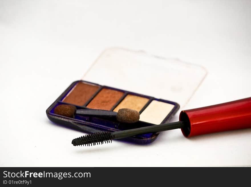 A close up of a mascara and eye shadow make up on a white background with natural shadows.