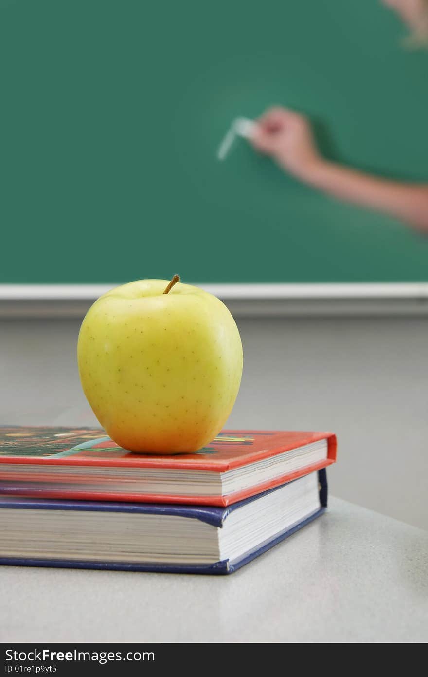 Books and apple, teacher wirting on the chalkboard. Books and apple, teacher wirting on the chalkboard.