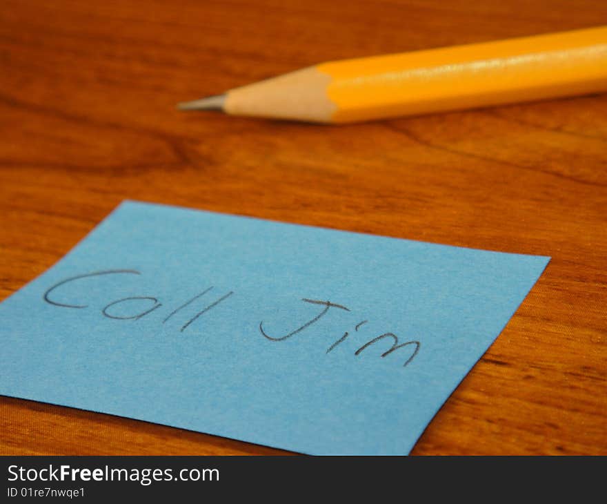 A sticky note that has Call Jim written on it with a pencil in the background on a desk. A sticky note that has Call Jim written on it with a pencil in the background on a desk.