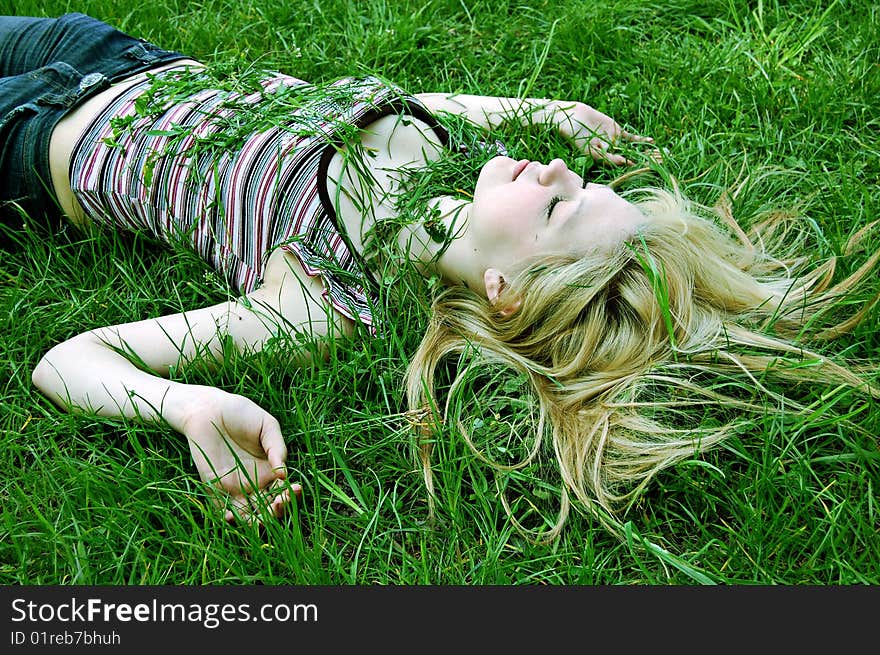 The young girl which lays in a green grass, the girl the blonde, a thin, green grass. The young girl which lays in a green grass, the girl the blonde, a thin, green grass