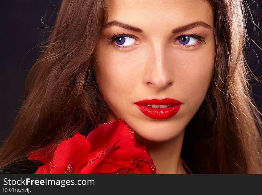 Portrait of a young beautiful brunettes with red lips in a black blouse decorated with a rose. Portrait of a young beautiful brunettes with red lips in a black blouse decorated with a rose