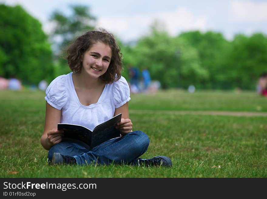 The girl with the open book sits on a grass and smiles. The girl with the open book sits on a grass and smiles