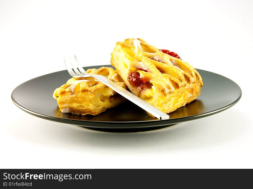 Raspberry and custard danish on a black plate with a fork on a white background. Raspberry and custard danish on a black plate with a fork on a white background